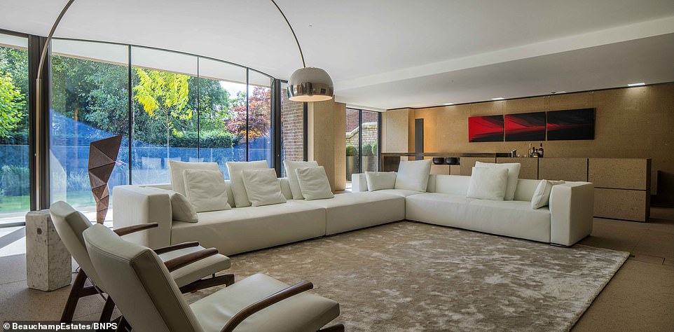 A Luxurious London House Living Area Boasts Curved Glass Walls, Flooding The Room With Light. A Plush White Sectional Sofa Anchors The Space, Complemented By Modern Art And Design.