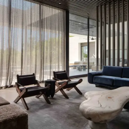 Modern Living Room In A Texas Hill Country Home With Sheer Curtains, Unique Wood Chairs, And A Blue Sofa. Large Windows Bring In Light.