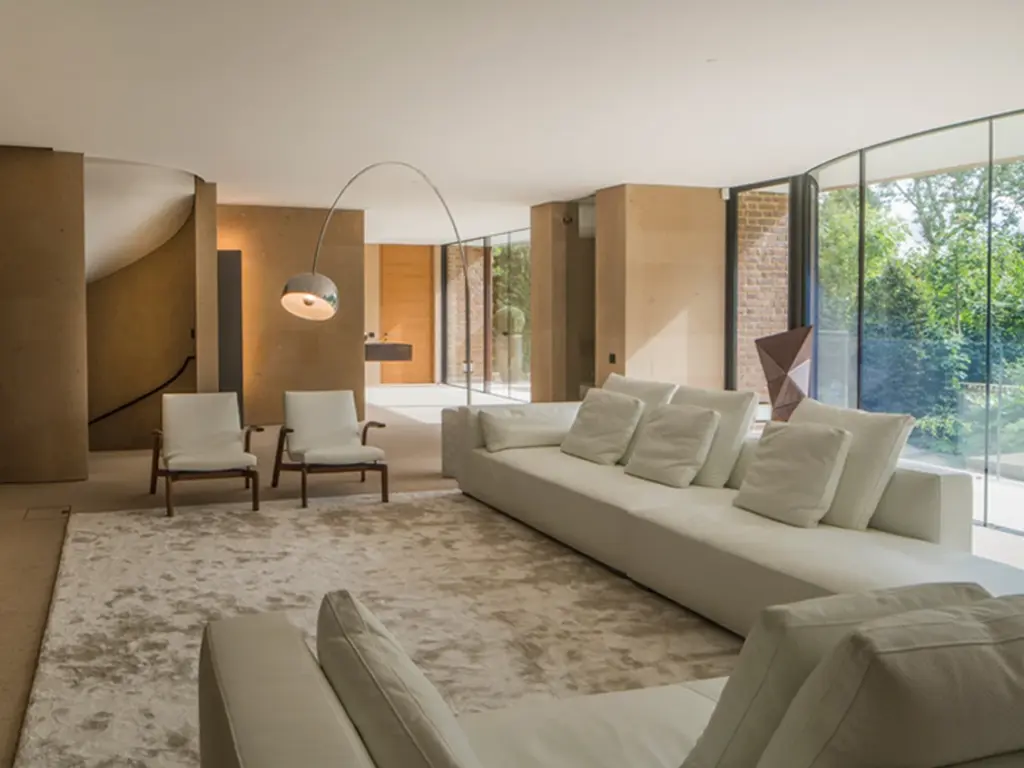 A Spacious London House Living Room With Curved Glass Walls, Flooding The Space With Natural Light. Neutral Tones, Plush Sofas, And A Minimalist Design Prevail.