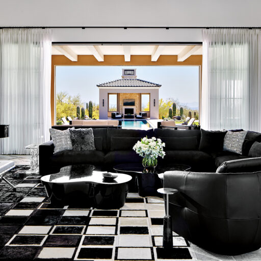 Elegant Mediterranean Home Living Room With Black Furniture, White Drapes, And A View To A Pool And Cabana. Black And White Patterned Rug Adds Contrast.