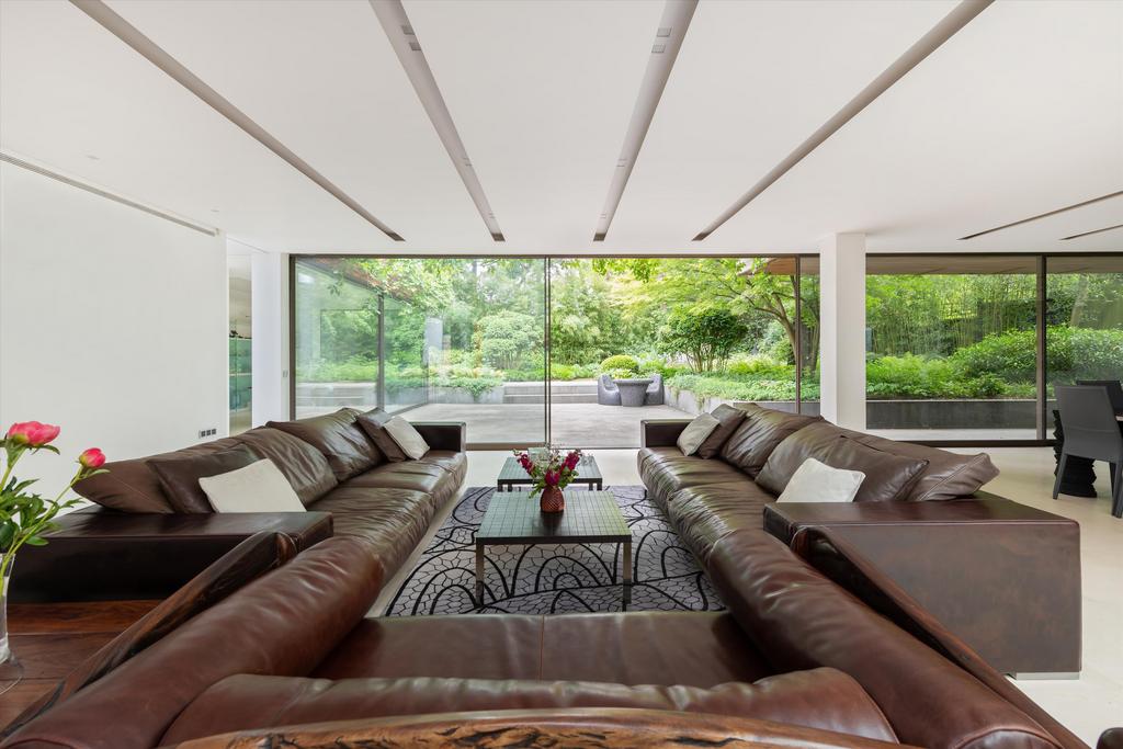 A Spacious London House Living Room With Symmetrical Brown Leather Sofas Facing Each Other. Floor-To-Ceiling Windows Open To A Lush Garden, Creating A Serene Indoor-Outdoor Flow.