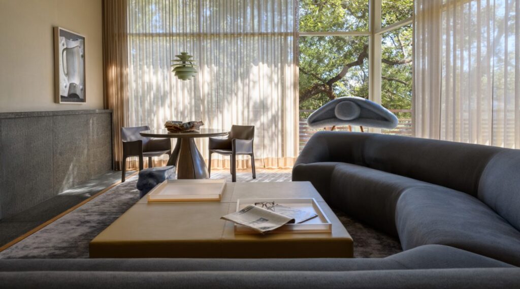 Living Area With Artisanal Unique Crafted Rug, With Large From Floor-To-Ceiling Windows, Centered Coffee Table, Comfortable Sofa And Home Plants